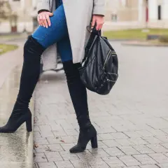 Kobieta w kozakach, które się nie ślizgają, na mokrym chodniku. Czarny plecak w dłoni.
