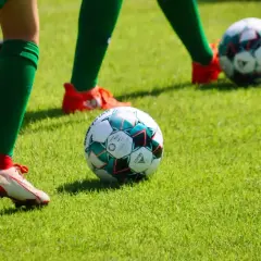 Piłkarze w zielonych getrach i czerwonych butach ćwiczą na boisku. Piłka leży na trawie, gotowa do gry.