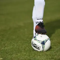 Piłkarz w białych getrach piłkarskich stawia stopę na piłce.