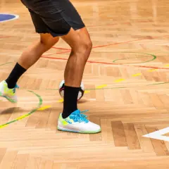 Gracz w butach na hale i orlik ćwiczy drybling na drewnianej parkietowej nawierzchni z zaznaczonymi liniami boiska.