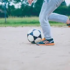 Chłopiec w dresach piłkarskich klubowych ćwiczy drybling na boisku.