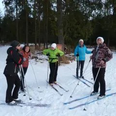 Grupa osób w strojach na narty biegowe przygotowuje się do jazdy w lesie.