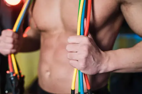 Mięśnie klatki piersiowej i ramiona mężczyzny podczas ćwiczeń na klatkę z gumami. Kolorowe gumy oporowe w dłoniach.