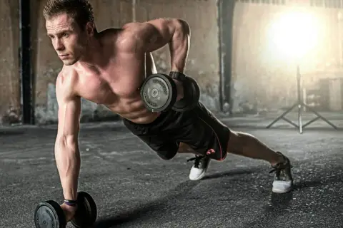 Mężczyzna wykonuje ćwiczenia na triceps z hantlami w pozycji deski. Intensywny trening buduje siłę.