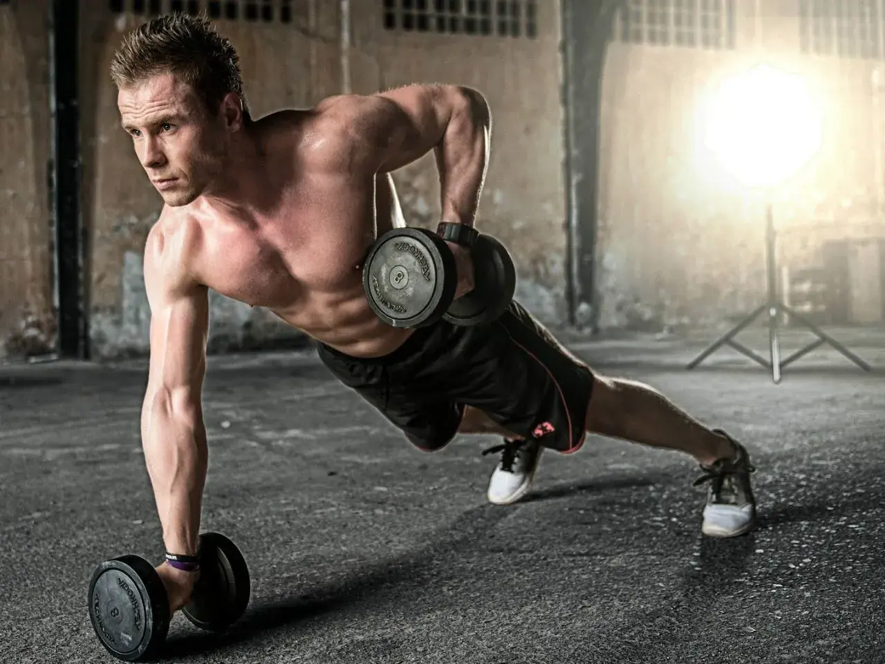Mężczyzna wykonuje ćwiczenia na triceps z hantlami w pozycji deski. Intensywny trening buduje siłę.