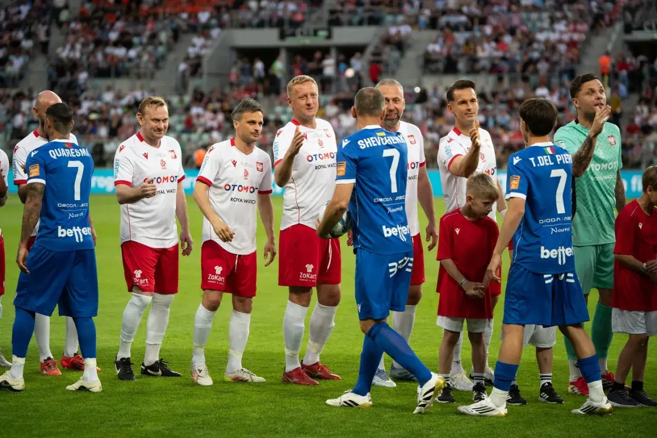 Grupa piłkarzy w białych strojach z godłem Polski i niebieskich, gotowa do meczu. Wśród nich lista polskich piłkarzy, jak Quaresma i T. Del Piero.