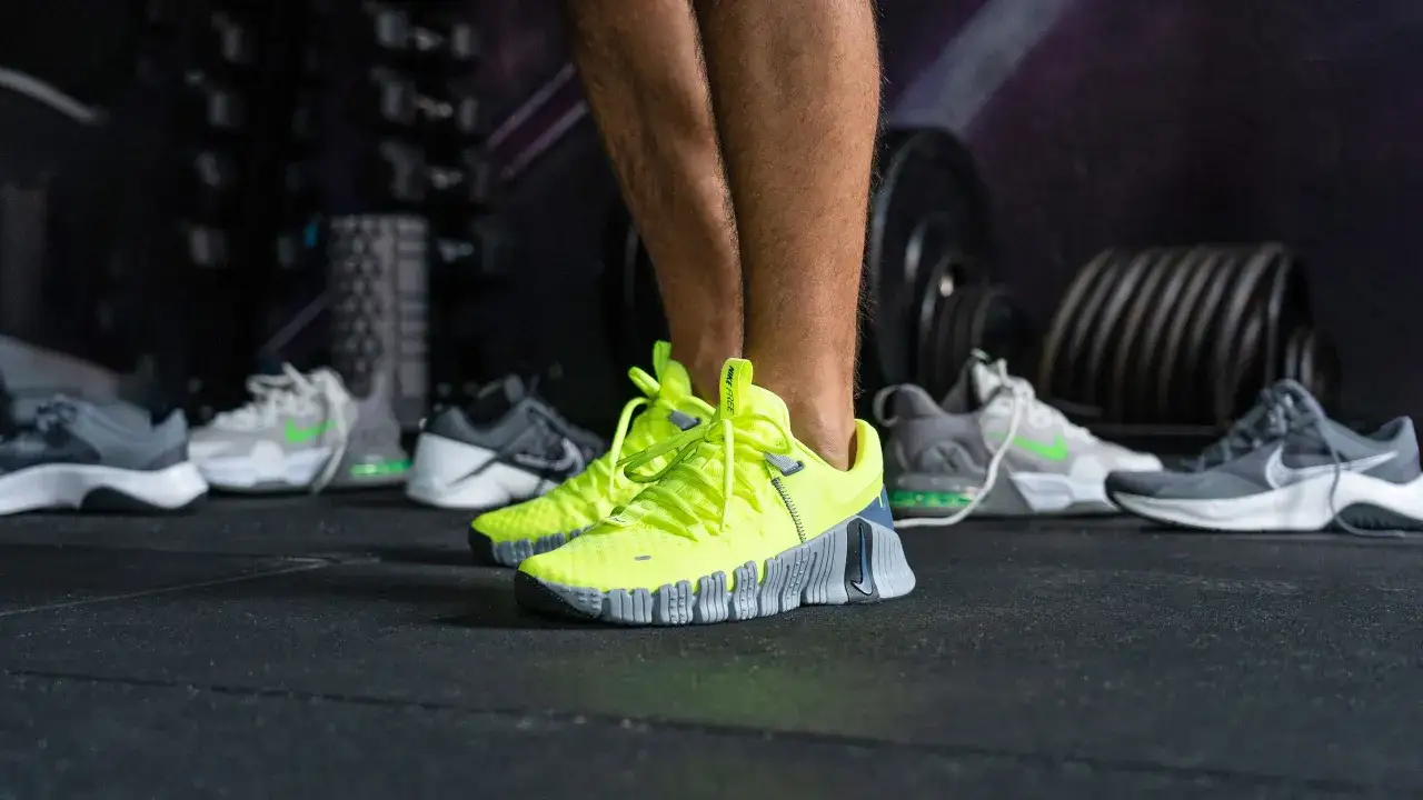 Jaskrawożółte buty Nike Free na siłowni, idealne do treningu. W tle inne modele butów sportowych.