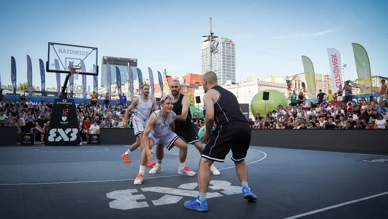 Zacięta gra w koszykówkę 3x3 na ulicznym boisku w Katowicach. Zawodnicy w akcji, tłum kibiców na trybunach.